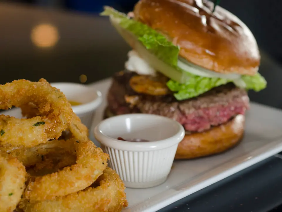 Hambúrguer de costela com alface ao lado de onion rings
